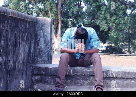 Depressiver Teenager, der allein an der Wand im Freien sitzt. Unangenehme Schmerzen. Traurig unglücklicher, gutaussehender Mann. Bangladesch und Asien leiden unter einer Depression. Stockfoto