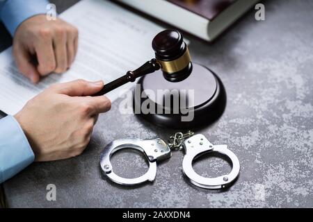 Nahaufnahme eines Richters Hand markante Hammer mit Handschellen auf dem Schreibtisch im Gerichtssaal Stockfoto
