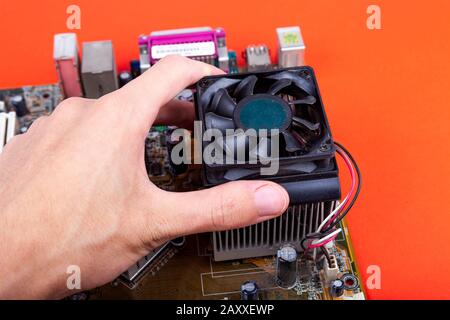 Entfernen eines kleinen alten CPU-Kühlers von der Hauptplatine. Die menschliche Hand entfernt einen veralteten, staubigen Lüfter und verbessert die Prozessorkühlung. Überhitzungsproblem des PCs Stockfoto