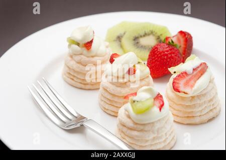 Baisse mit kleinen, individuellen, cremefarbenen Meringues und Kiwi-Obst und Erdbeeren Stockfoto