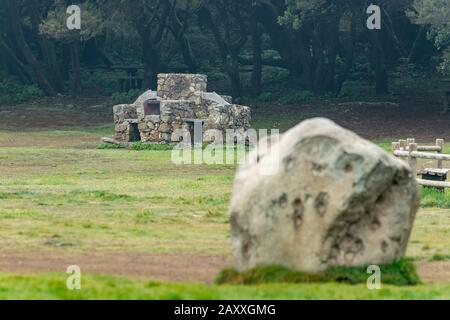 Selektiver Fokus. Grill zum Kochen. Bänke, ein Holztisch für Speisen im einzigartigen Wald im Hintergrund. Riesiges Basaltgestein aus Stein im B. Stockfoto