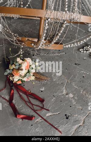 Ringe der Neuvermählten auf grauem Grunge und Hintergrund eines Blumenstraußes von Bräuten. Ringe und brautstrauß vor dem Hintergrund eines Chic, l. Stockfoto