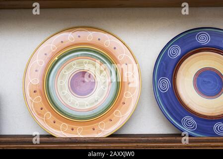 Bunte gemusterte Keramikplatten für Abendessen auf einem wandmontierten Holzregal in Nahsicht Stockfoto