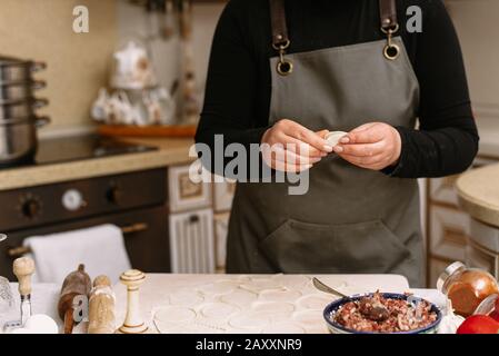 Eine Frau in der Küche schimpft hausgemachte Knödel oder Halbfertigprodukte. Der Koch wickelt das Hackfleisch aus Rindfleisch in den Teig. Stockfoto