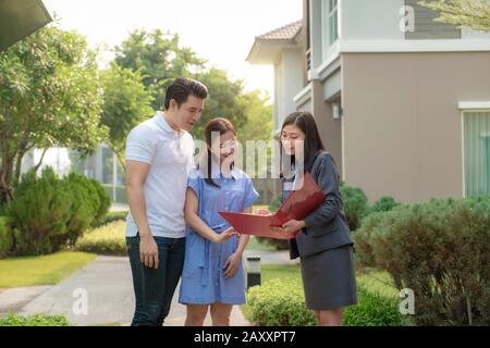 Asian Woman Immobilienmakler, die dem jungen asiatischen Liebespaar, der es sucht und Interesse daran hat, es zu kaufen, ein Detail in ihrer Akte zeigt. Ein neues h kaufen Stockfoto