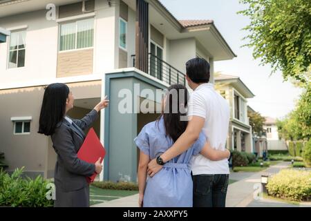 Asian Woman Immobilienmakleragentin, die dem jungen asiatischen Liebespaar, der es sucht und Interesse daran hat, ein Hausprojekt in ihrer Akte ausführlich zeigt. Kaufen Stockfoto