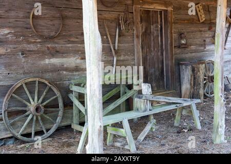 Holzbank und Rad auf der Vorhalle eines alten Blockhauses in Washington, Georgia. Dieses Blockhaus wurde in den Pioniertagen Amerikas gebaut. Stockfoto