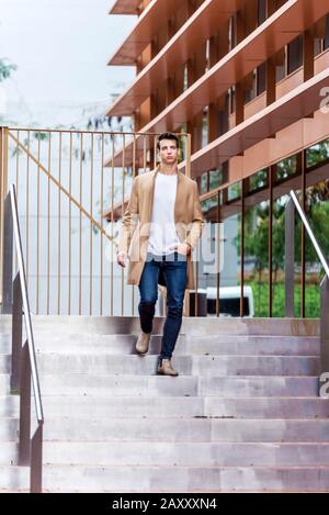 Ein junger Mann steigt an der Treppe in der Stadt herab und trägt einen Mantel. Modisch gekleideter Kerl. Lebensstil Stockfoto