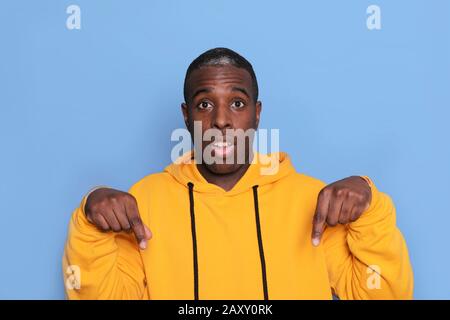 Horizontaler Schuss des afroamerikanischen jungen Mannes zeigt beide Zeigefinger nach unten, Stockfoto