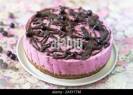 Rosafarbener Vegankuchen mit Cashewnüssen und Waldfrüchten mit roher veganer Schokolade mit Aronia-Beeren. Stockfoto