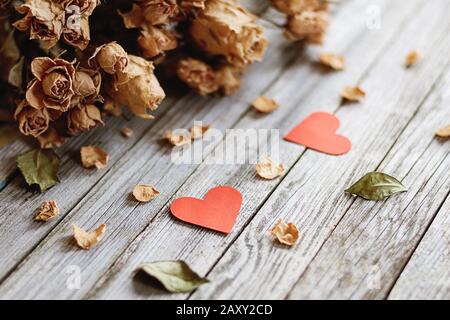 Erinnerungen an romantische Liebe. Zwei rote Herzen und ein getrockneter Rosenstrauß auf grauem Holz Stockfoto