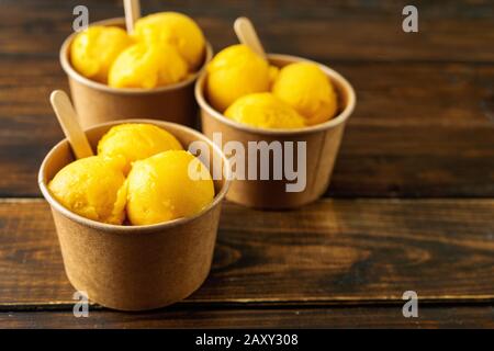 Drei Papierbecher mit Mango-Sorbet auf rustikalem Hintergrund Stockfoto
