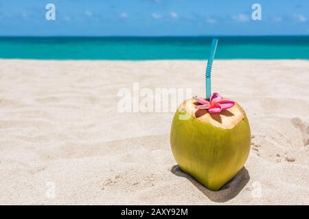 Frische, junge Kokosnuss auf dem Sandstrandgrund mit trinkbereitem Strohhalm. Tropisches Urlaubsreisekonzept. Kopierbereich. Weisses Sandy Ziel. Stockfoto