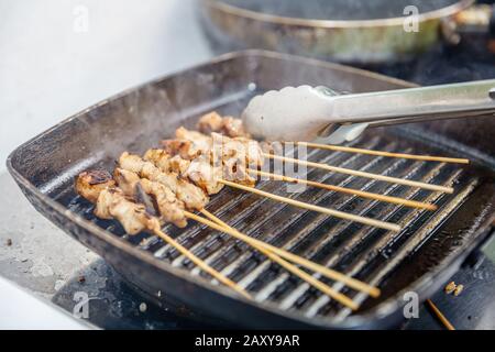 Sate Ayam - gegrilltes Hühnerfleisch auf Holzspießen, die auf einer gegossenen Pfanne zubereitet werden. Indonesische Küche. Stockfoto