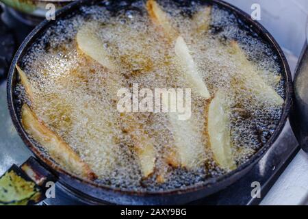 Gewürzte Kartoffelkeile, die in heißem Öl auf einer gusseisernen Pfanne braten. Prozess. Stockfoto