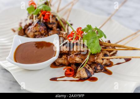 Sate Ayam - gegrilltes Hühnerfleisch auf Holzspießen serviert mit Sambalkakang - Erdnusstauchsauce auf einer Keramikplatte. Indonesische Küche. Stockfoto