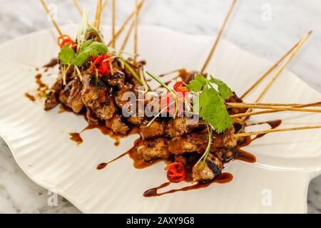 Sate Ayam - gegrilltes Hühnerfleisch auf Holzspießen serviert mit Sambalkakang - Erdnusstauchsauce auf einer Keramikplatte. Indonesische Küche. Stockfoto