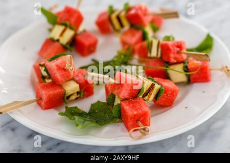 Vorspeise mit roter Wassermelone, frittiertem Hallumi-Käse und Minze auf Spießen auf weißem Keramikplatte. Stockfoto