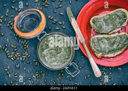 Hausgemachte vegane Kürbissaatbutter in einem kilner Glas und auf einem weißen Sauerteig Brot auf einem Schiefergrund verteilt Stockfoto