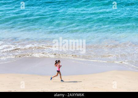 Frau Läuferin trainiert Kardio am Meer am Strand. Morgendliches Workout. Copyspace auf blauem Wasser. Stockfoto
