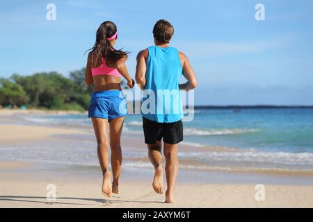 Zwei Fitness-Athleten laufen am Strand zusammen. Leute von hinten joggen barfuß auf Sand am tropischen Reiseziel. Gesunde Passform junge Erwachsene mit muskulösen, schlanken Beinen trainieren Kardio. Stockfoto