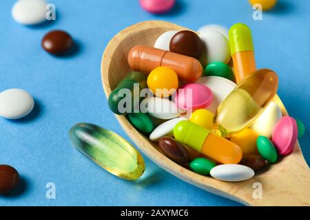 Holzlöffel voller Pillen, Tabletten, Vitamine, Medikamente, Omega-3-Fischöl, Gelkapseln, Medikamente und Nahrungsergänzungsmittel für die Gesundheit. Blauer Hintergrund. Stockfoto