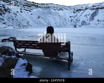 Ein Kerl sitzt auf einer Bank, die in Lake Kerid im Krater eines erloschenen Vuklan gefroren ist. Wunder von Island im Winter. Stockfoto