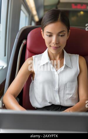 Junge chinesische Geschäftsfrau, die E-Mails auf dem Computer schreibt, während sie morgens zur Arbeit pendelt. Pendlerfrau sitzt im Hochgeschwindigkeitszug auf dem Sitz der Business-Klasse. Reisen in die Stadt. Stockfoto