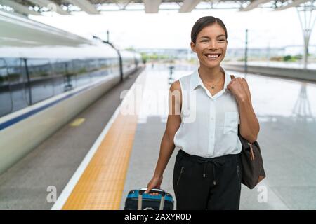 Geschäftsfrau am Bahnhof am Zielort mit Handgepäck. Glückliche Asianerin auf dem Weg zur Arbeit in der Stadt. Stockfoto