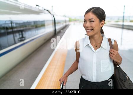 Fröhlicher asiatischer Reisender lächelt auf Zugfahrt in der Business Class. Schöne Frau mit Handgepäck, die auf Luxustransporte abreisen kann. Geschäftsfrau, die morgens zur Arbeit pendelt. Stockfoto