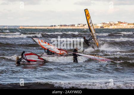 Tallinn, Estland - 18. Oktober 2008: Vier Windsurfer im Meer versuchen zu reiten. Der Himmel ist bewölkt. Der Ozean erschüttert. In der Ferne ist ein verschwommenes Land Wi Stockfoto