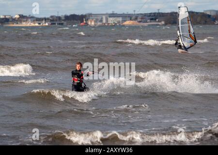 Tallinn, Estland - 18. Oktober 2008: Kitesurfer und Windsurfer fahren bei windigem Wetter auf dem Meer. Meer mit Wellen. Verschwommener Landstreifen mit Gebäuden Stockfoto