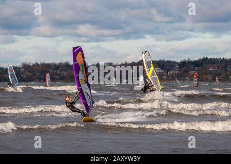 Tallinn, Estland - 18. Oktober 2008: Windsurfer in Anzügen fahren bei windigem Wetter auf dem Meer. Meer mit Wellen. Verschwommener Landstreifen mit Gebäuden o Stockfoto