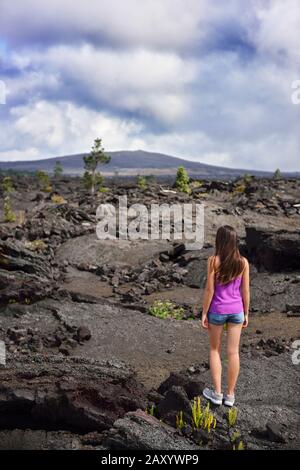 Frau, die in vulkanischen Felsen auf dem Vulkan der großen Insel Hawaii, USA, wandert. Touristengeher, die während der Sommerferien auf vulkanischen schwarzen Felsen spazieren. Stockfoto