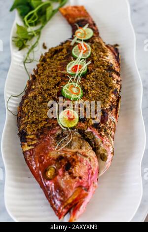 Ganze gegrillte Schnapperfische werden auf einer weißen Keramikplatte serviert. Dekoriert mit Kalk und geschnittenen Chili. Draufsicht. Stockfoto