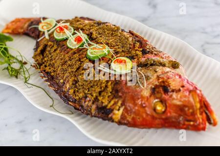 Ganze gegrillte Schnapperfische werden auf einer weißen Keramikplatte serviert. Dekoriert mit Kalk und geschnittenen Chili. Draufsicht. Stockfoto