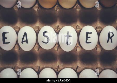 Festliche Ostereier im Karton mit Text. Ostertext auf weißen Eiern geschrieben. Fröhliches Osterfest, Frühlingsfesttage auf farbenfrohem Hintergrund Stockfoto