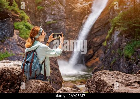 Glückliche Reisende Frau, die ein Foto von einem majestätischen Wasserfall im Dschungel macht. Wander- und Sightseeing-Konzept Stockfoto