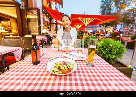 Ein asiatisches Mädchen trinkt einen Becher Lagerbier in einem traditionellen bayerischen Restaurant und Snacks auf einem frischen Salat. Deutsches Delikatessenkonzept Stockfoto