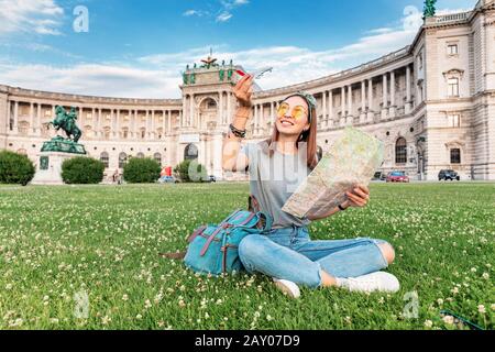 19. Juli 2019, Wien, Österreich: Glückliche asien-frau-Reisende mit Karte auf einem grünen Rasen in der Wiener Stadt am Hofburg Stockfoto