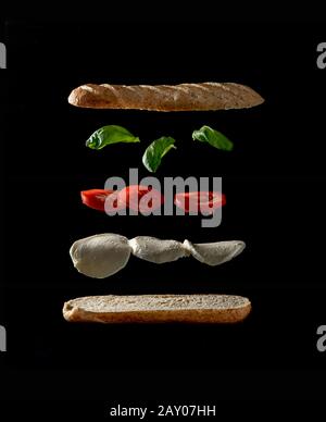 Levittierende Zutaten eines leckeren Veggie-Sandwiches auf schwarzem Hintergrund Stockfoto