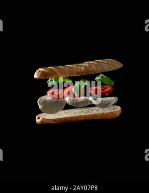 Levittierende Zutaten eines leckeren Veggie-Sandwiches auf schwarzem Hintergrund Stockfoto