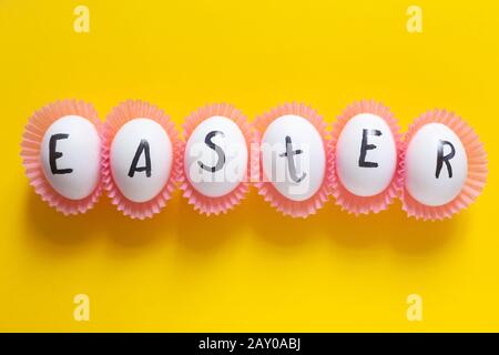 Helles Osterbild mit weißen Eiern auf gelbem Hintergrund. Weiße Eier mit Text - Ostern auf dem bunten Hintergrund Stockfoto