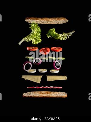 Levittierende Zutaten eines leckeren Veggie-Sandwiches auf schwarzem Hintergrund Stockfoto