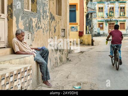 DIU, Indien - Dezember 2018: Ein alter Mann sitzt in einer schlampigen Haltung außerhalb eines Hauses auf den ruhigen Straßen der Insel Diu. Stockfoto