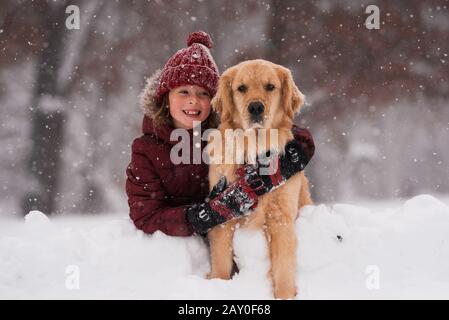 Mädchen, die im Schnee sitzen und ihren goldenen Hund aus Retriever, Wisconsin, USA, kuscheln Stockfoto