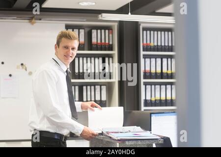 Lächelnder Verkäufer steht im Büro eines Ladens und betrachtet eine Broschüre, Deutschland Stockfoto