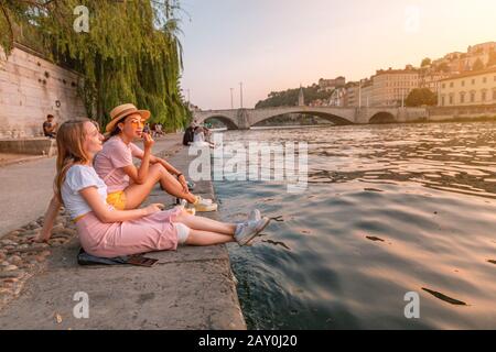 Zwei glückliche kaukasische und asiatische Mädchen-Freunde treffen auf einem Fluss Saone in der Stadt Lyon großen Sonnenuntergang. Reisen und Lifestyle in Frankreich Stockfoto