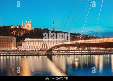 Stadtbild der Nacht von Lyon mit beleuchtetem Courthouse und roter Fußgängerbrücke über den Fluss Saone. Panorama-Blau-Stundenlandschaft Stockfoto