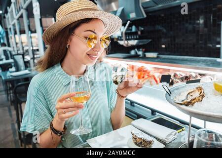 Asiatische Frau schmeckt frischen Rohauster und trinkt Wein im Fischrestaurant Stockfoto